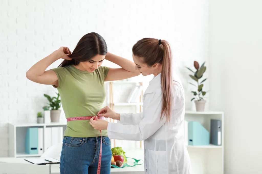 A doctor measuring a patient's waist during a medical weight loss consultation.