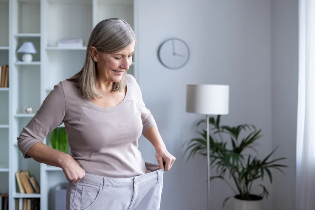 A happy woman showing her loose pants after successful medical weight loss results.