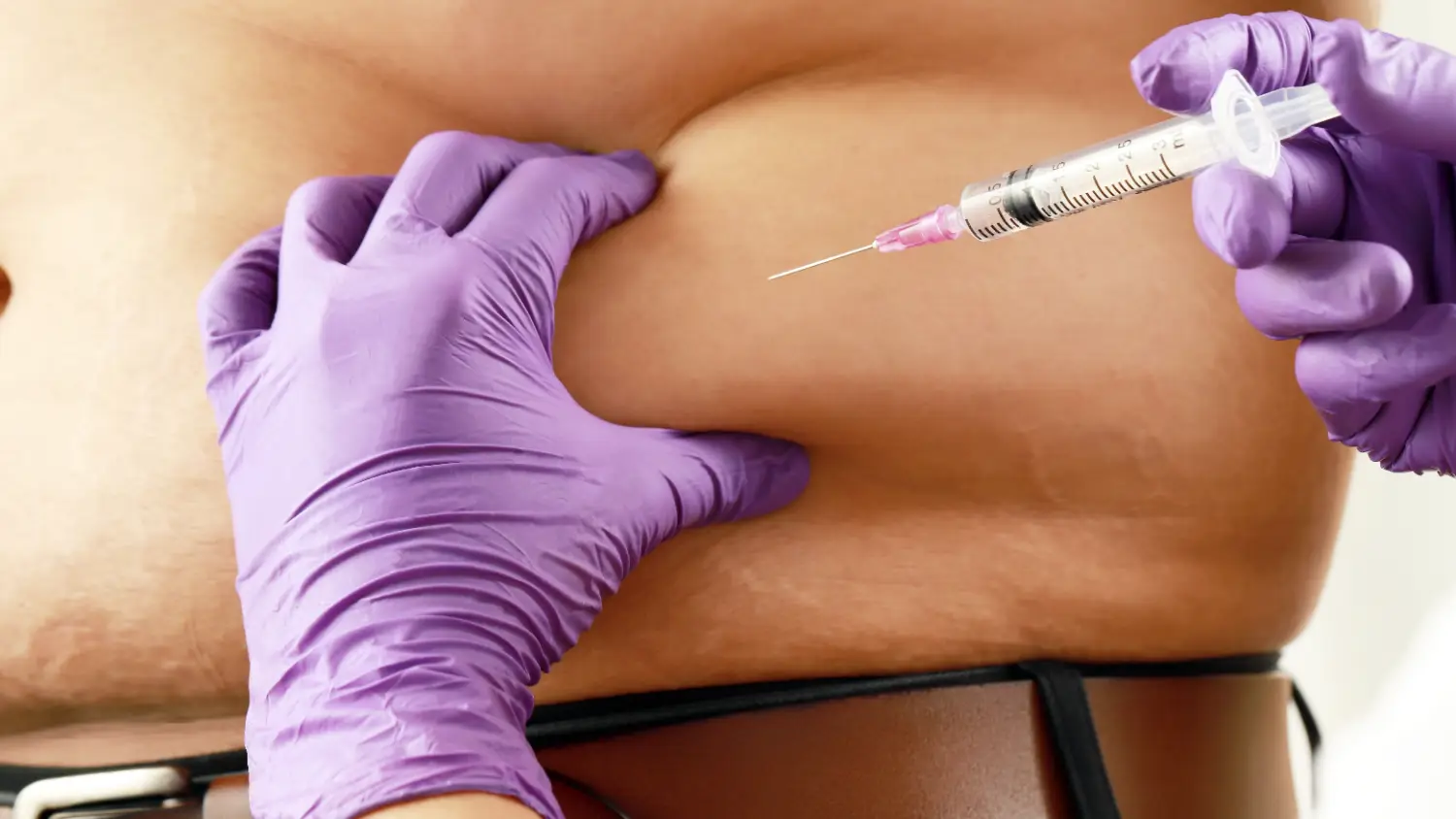 Gloved hands holding a syringe near skin on a person’s abdomen