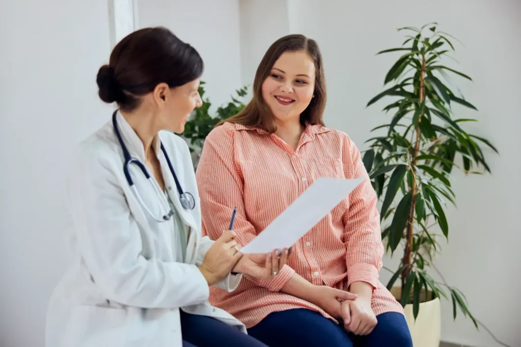 Doctor with stethoscope reviewing a document with a seated woman in a clinic office