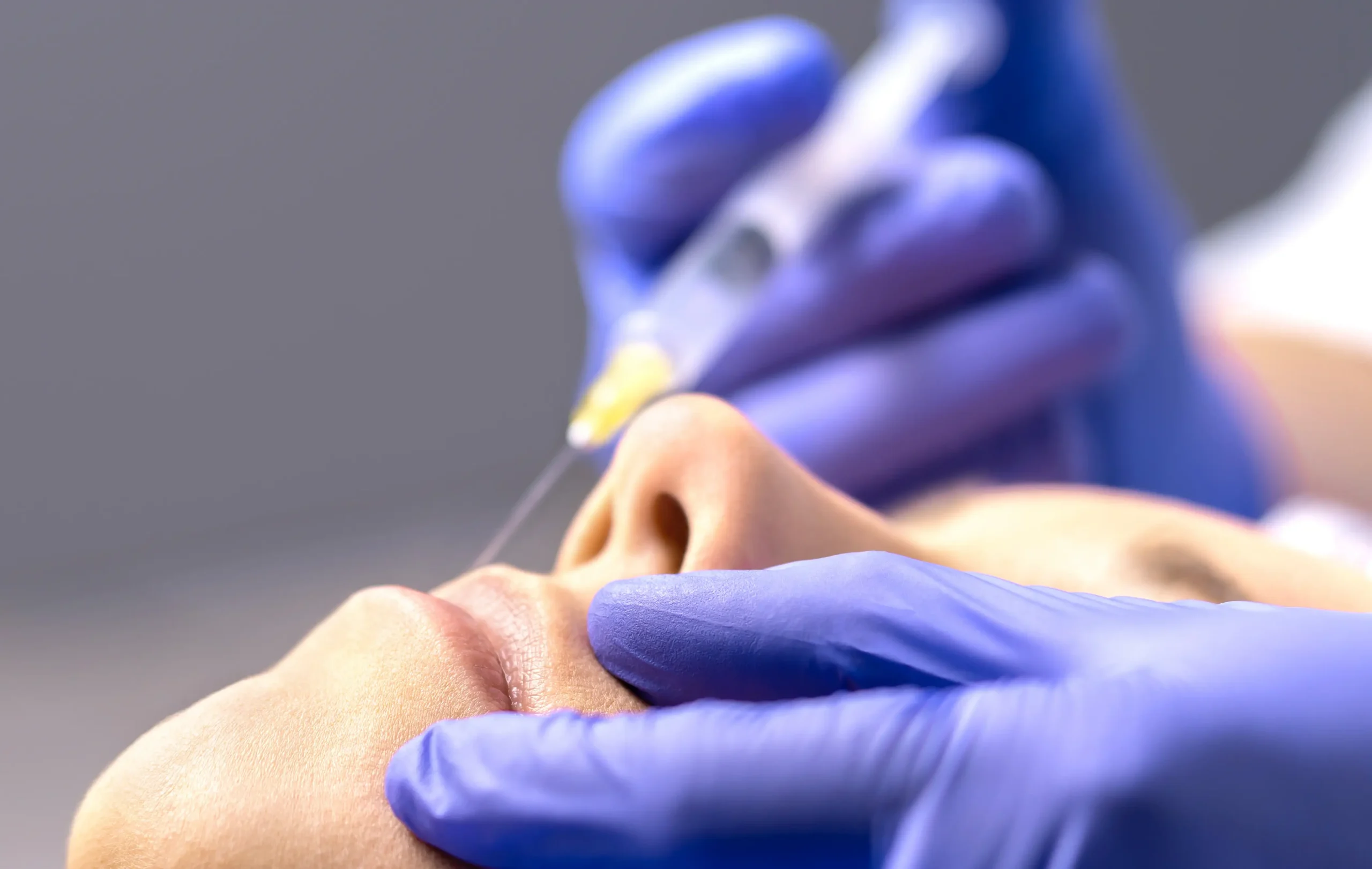 Close-up of facial injection procedure with gloved hands and syringe