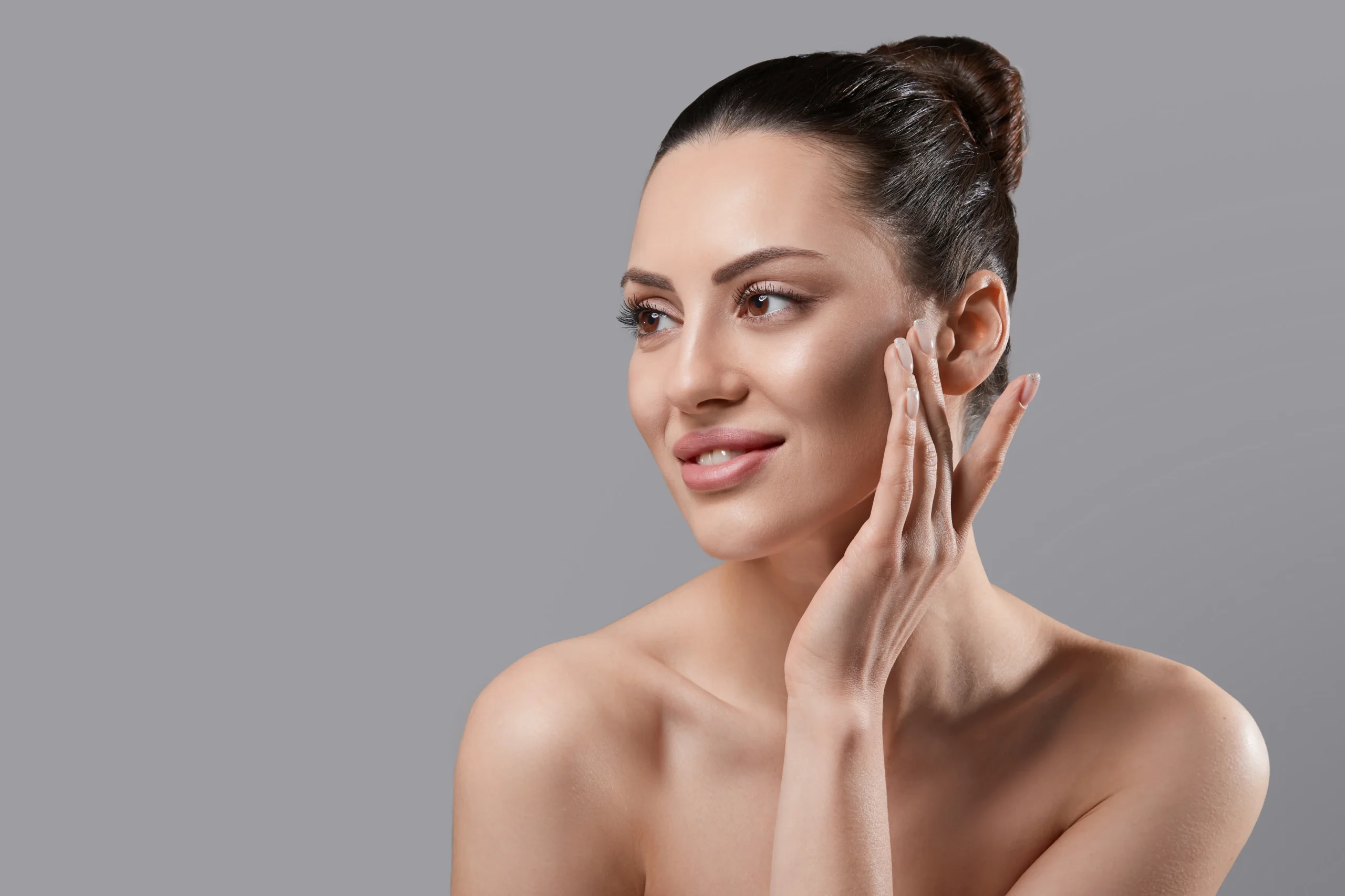 Woman touching cheek with smooth glowing skin against gray background