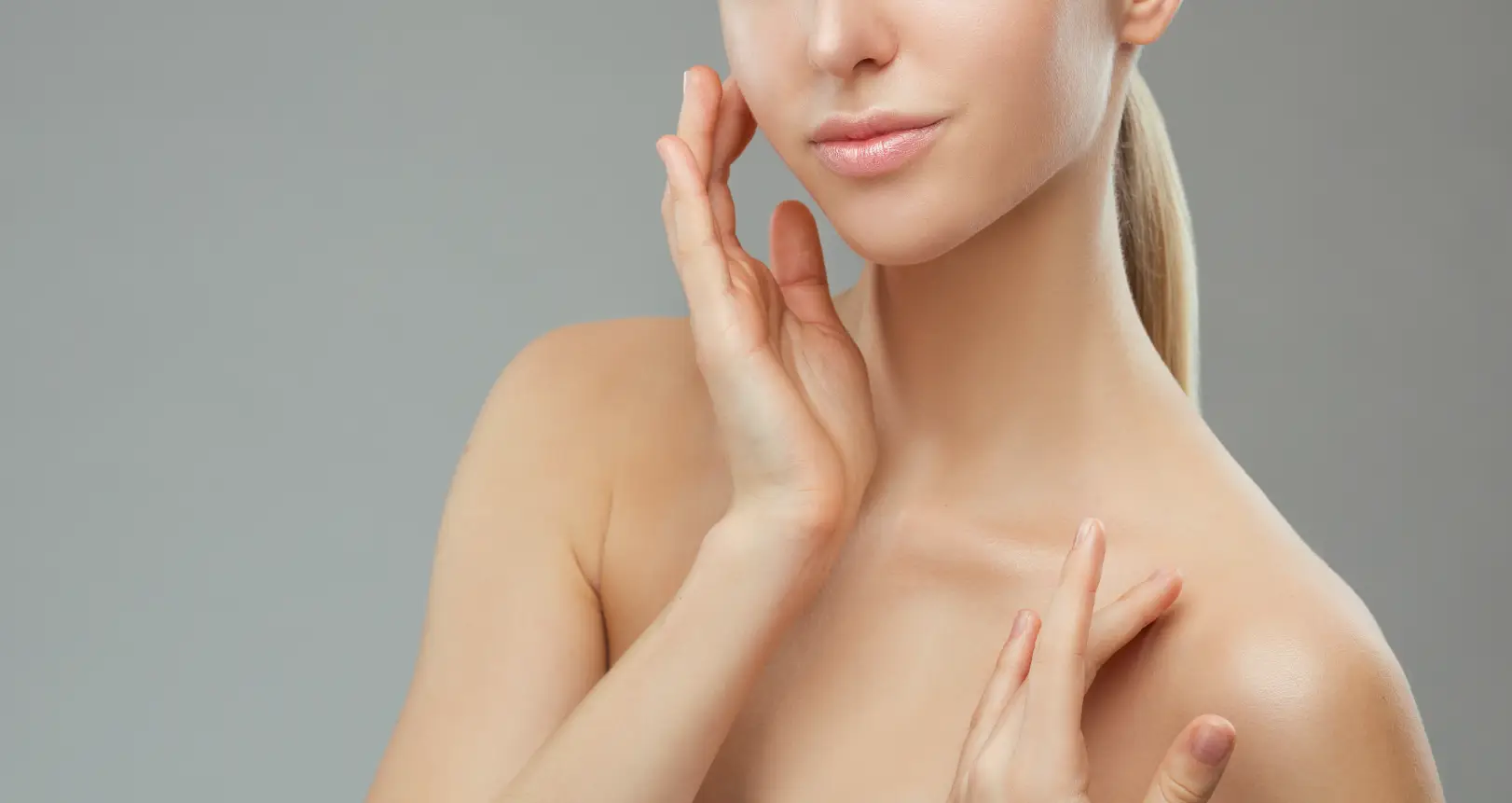 Woman touching her face and neck against a neutral background.