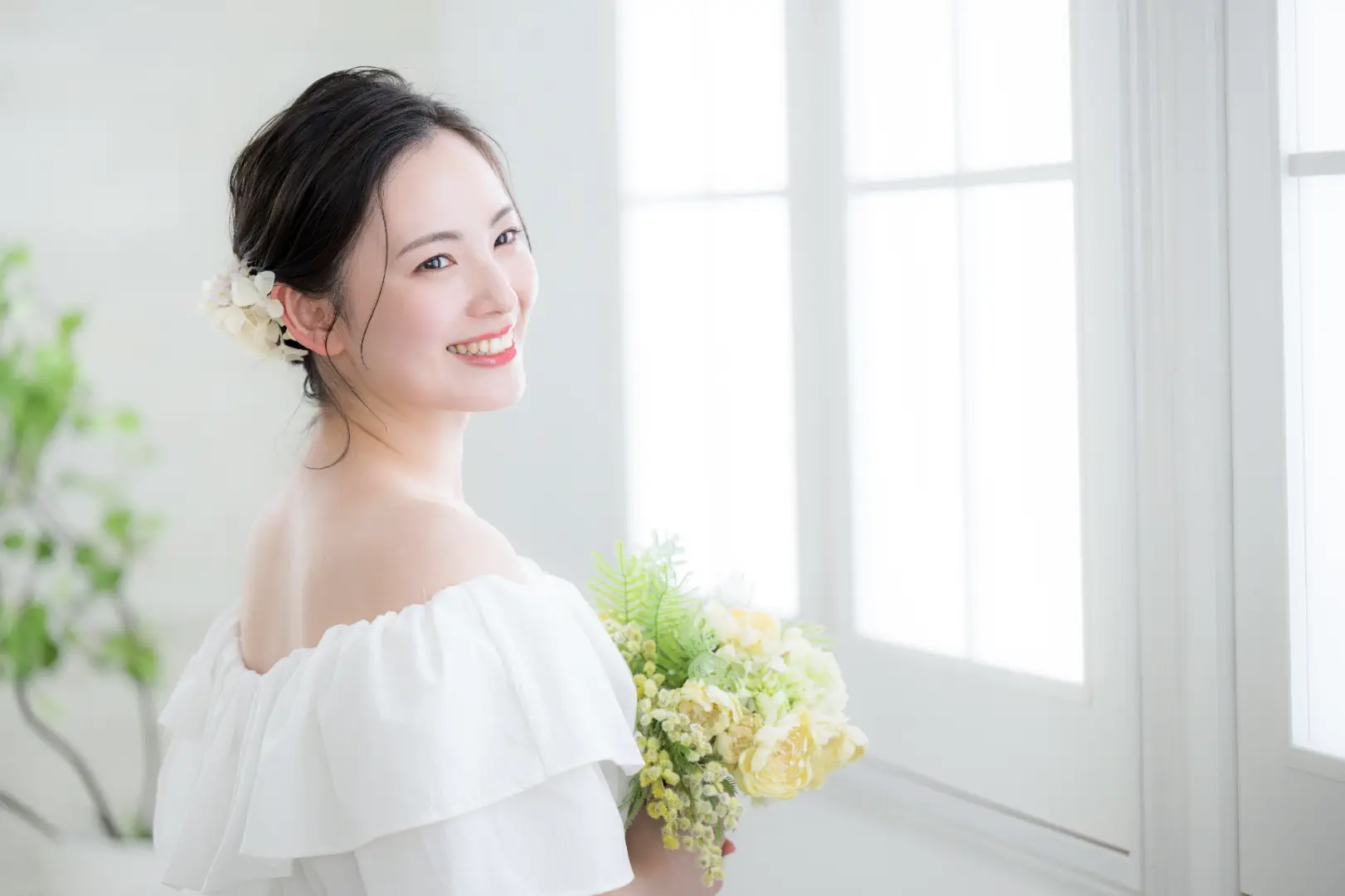 Woman holding a bouquet and smiling near a bright window indoors.