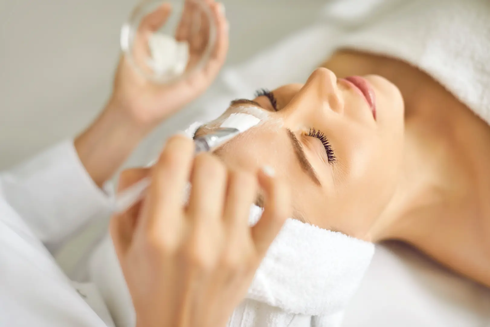 Esthetician applying a facial mask to a person's forehead during a skincare treatment.