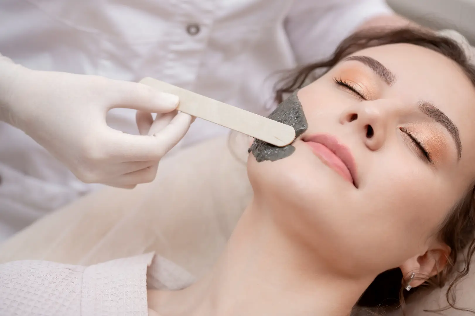 Woman receiving a facial mask treatment while lying on a spa bed.