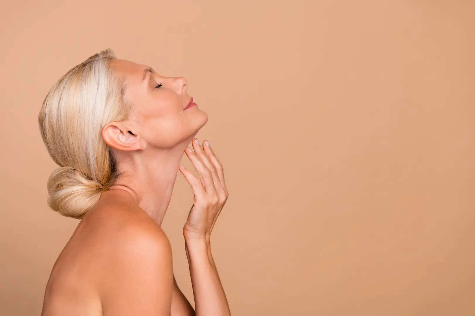 Woman with eyes closed touching her neck against a beige background.