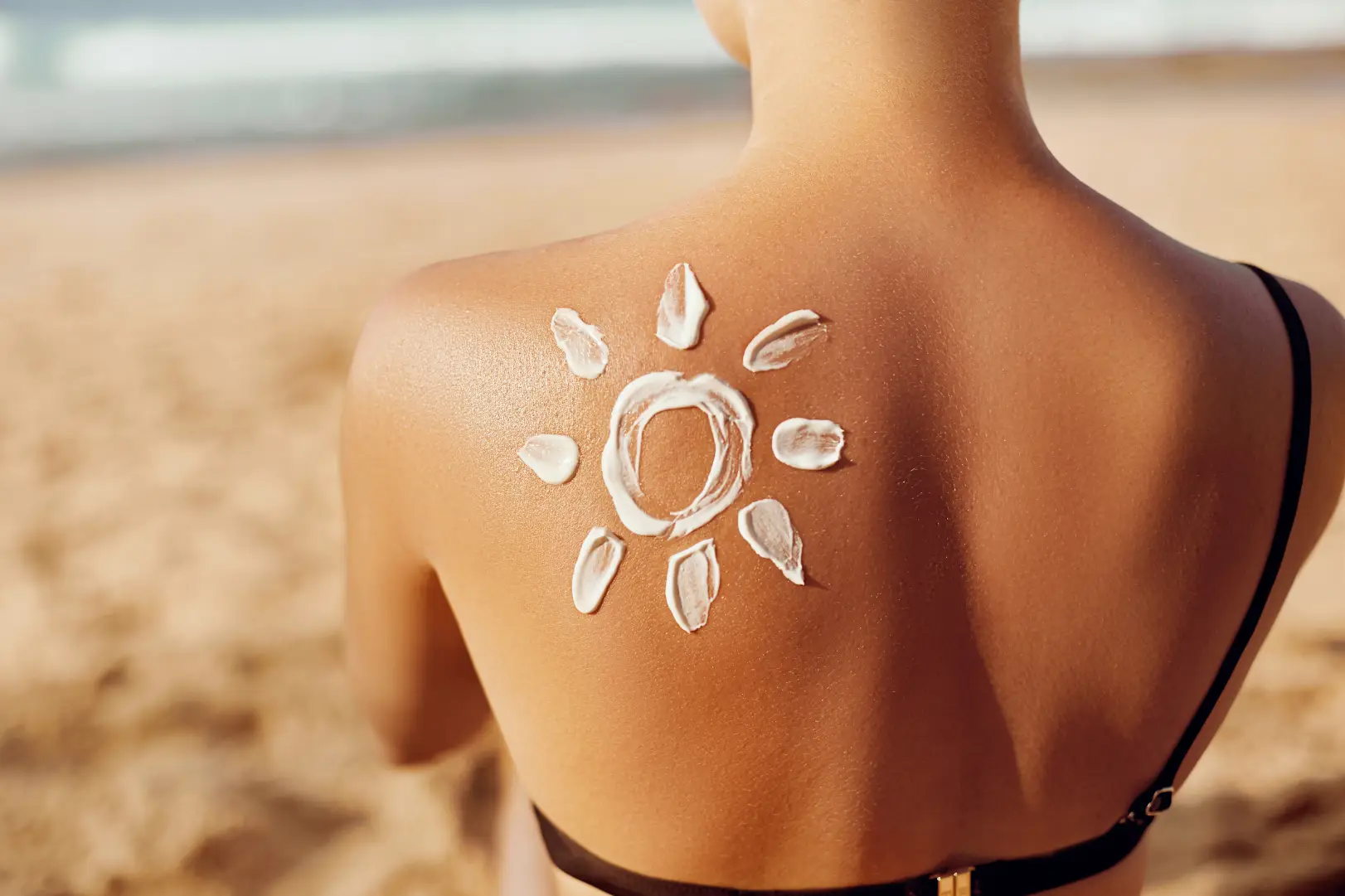 Sunscreen applied in a sun shape on a person's back at the beach.