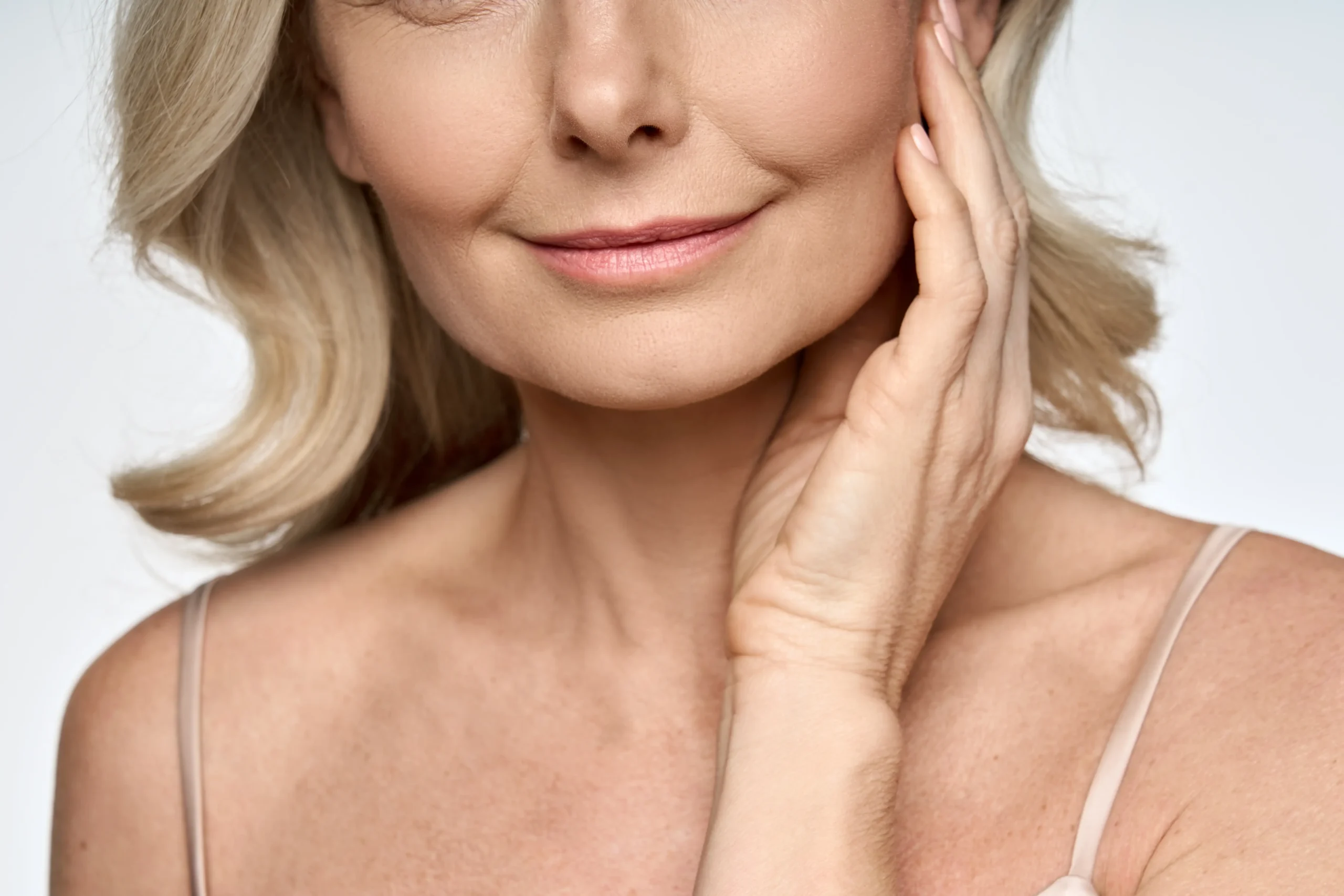 Close-up of a mature woman touching her cheek while smiling gently.